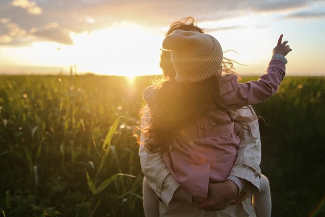 Mother holding child in arms amongst the sunset